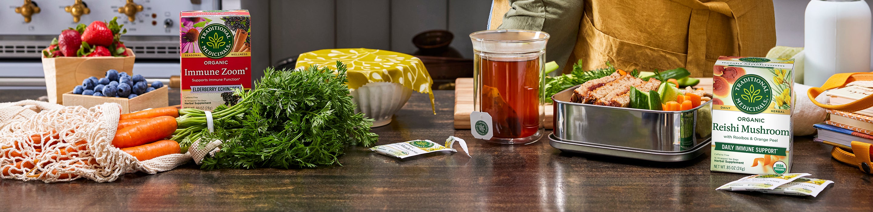 Tea boxes, herbs, brewed tea, fruits and veggies on kitchen counter