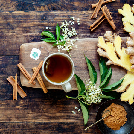 A cup of Cold Care P.M.® Tea on a wooden board surrounded by cinnamon sticks, ginger slices, and herbs promises a good night's sleep.