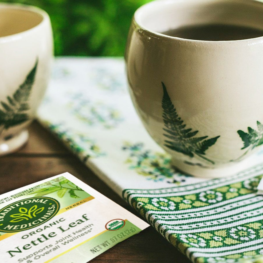 Two cups of herbal tea sit on a patterned cloth next to a package of Nettle Leaf Tea, highlighting its benefits for joint health and overall wellness.