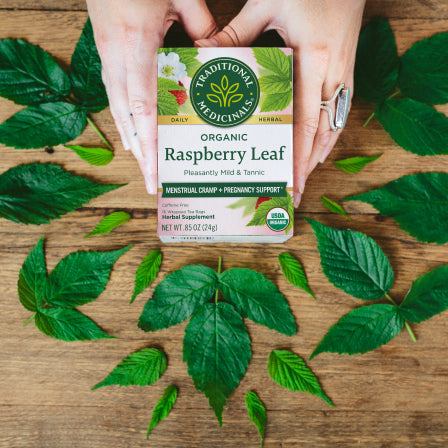 A box of Raspberry Leaf Tea rests on a wooden surface, surrounded by lush green leaves. Celebrated for its ability to ease menstrual cramps and support a healthy pregnancy, this blend delivers natural comfort and wellness in every cup.