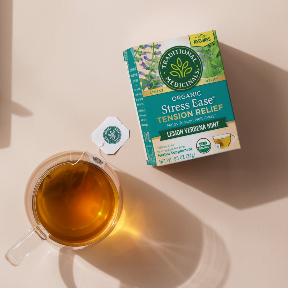 Box of Stress Ease® Tension Relief Tea with a cup of lemon verbena mint tea on a beige surface, providing peaceful moments.