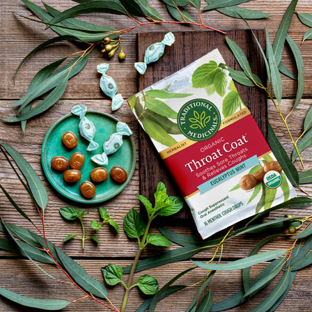 Box of Throat Coat® Eucalyptus Mint Lozenges, 30ct, featuring eucalyptus, mint, and soothing menthol flavors, beautifully arranged with leaves and candies on a wooden table—ideal for relieving sore throats.